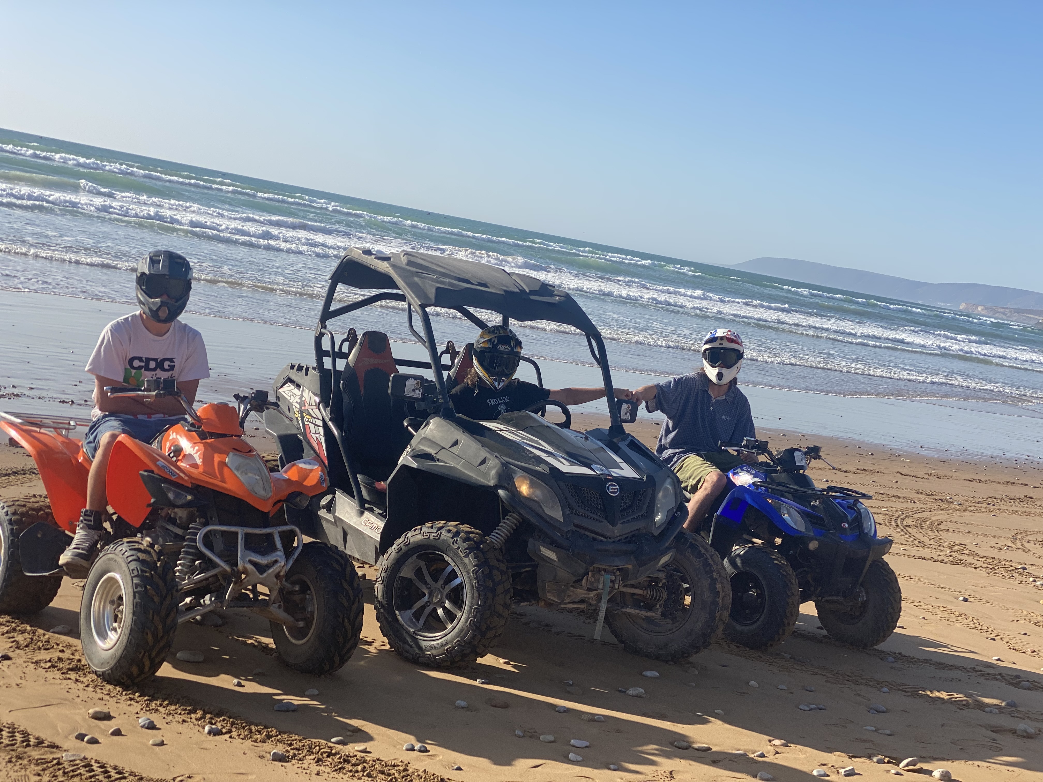 Three people on ATVs celebrating sunset on beach